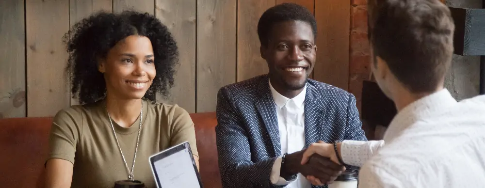 Young a couple shaking hands with businessperson.